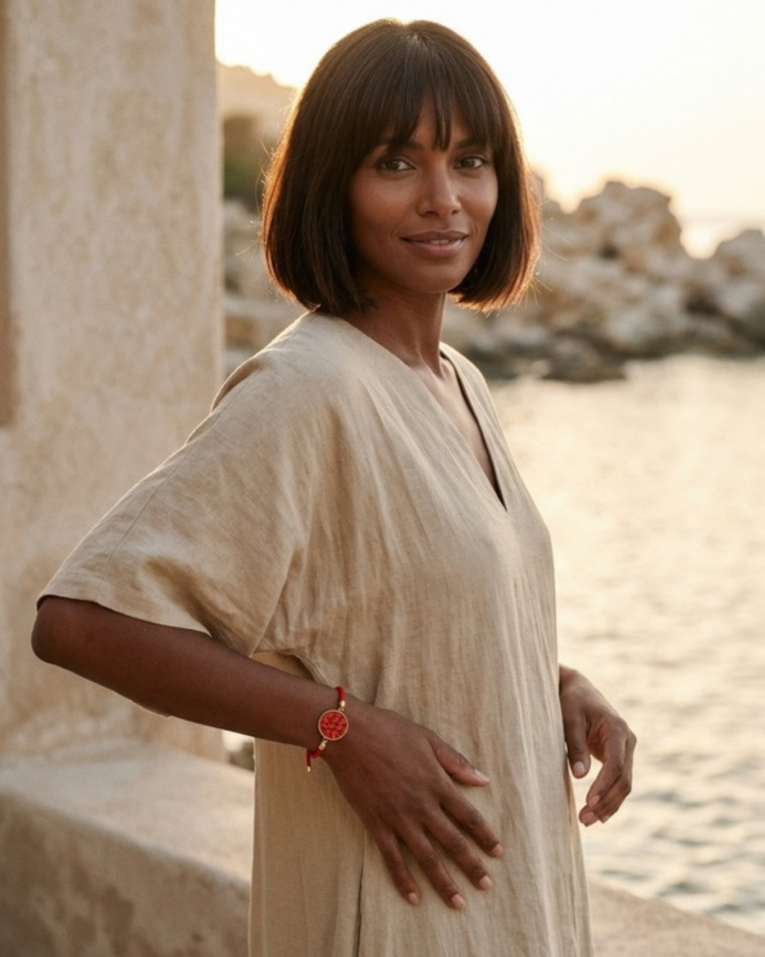 Femme portant le bracelet Andréa, cordon rouge et médaillon en cuir marin Terracotta, au bord de la mer