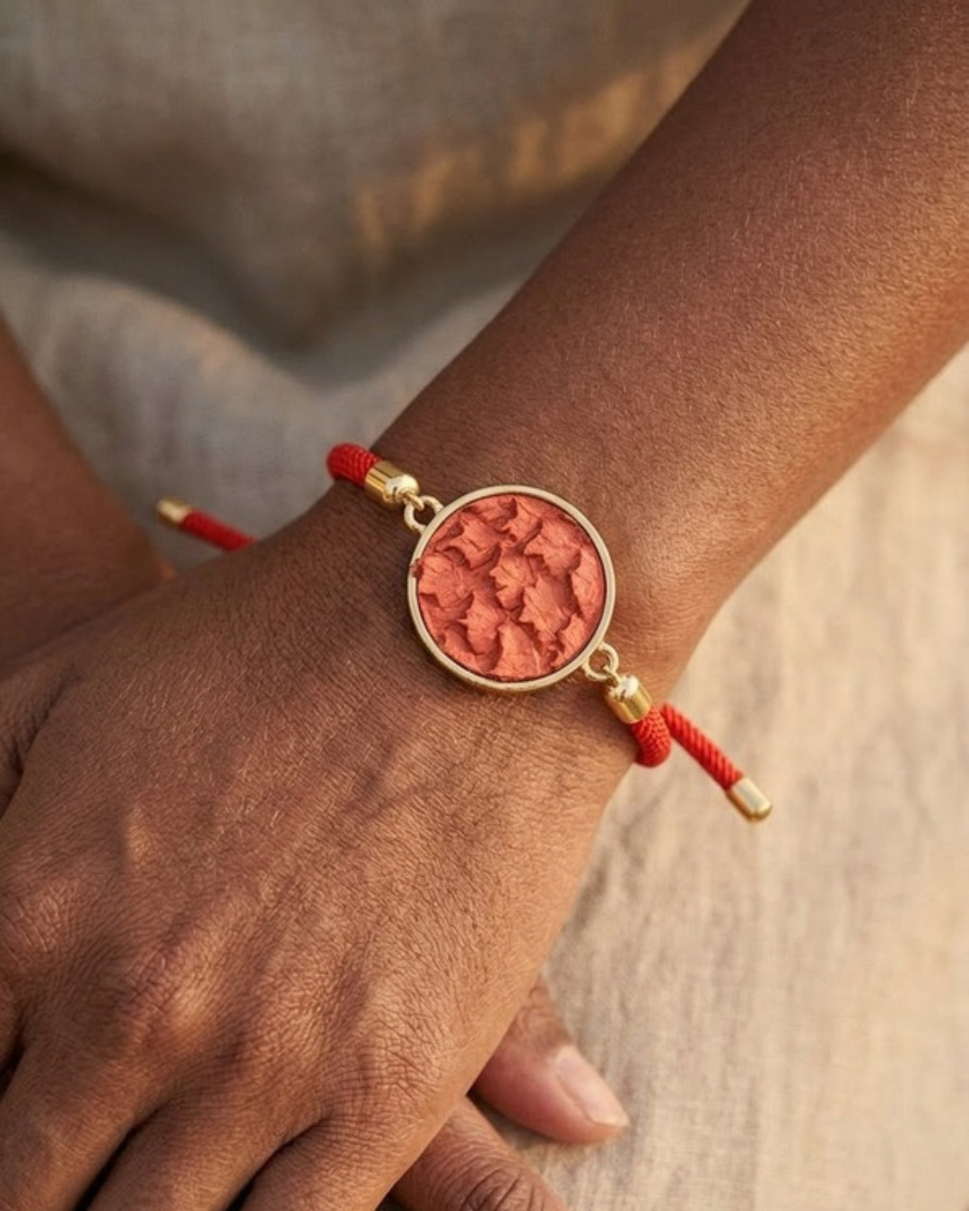 Gros plan sur le poignet : bracelet Andréa, médaillon rond en cuir de poisson Terracotta et cordon rouge coulissant